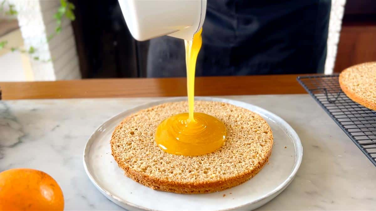 pouring orange curd onto the cake
