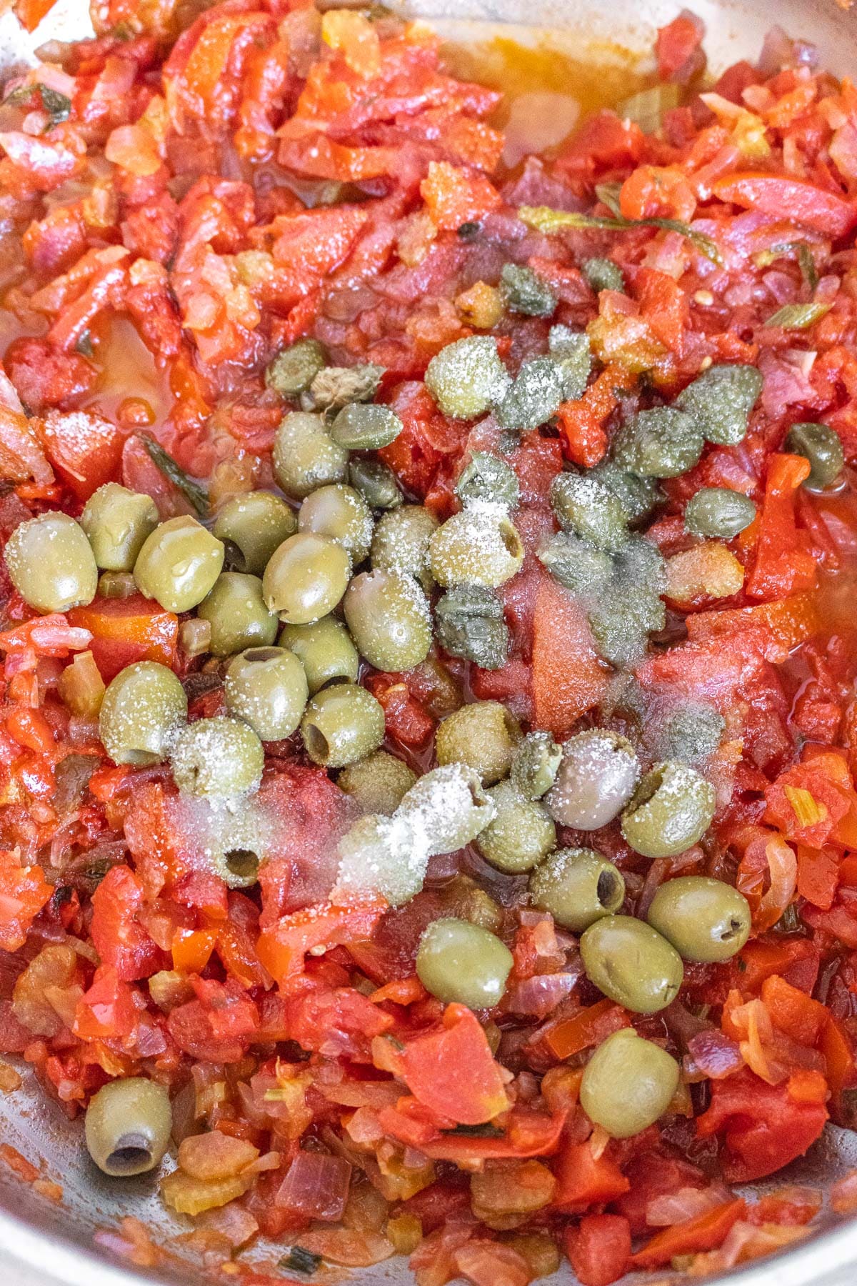 adding tomatoes, olives, and capers to the pan