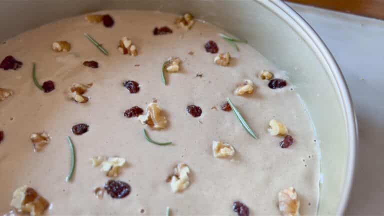 cake batter in a pan with raisins and walnuts on top