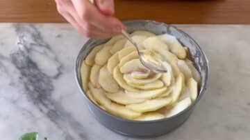 covering the vegan apple cake with apple slices and sugar