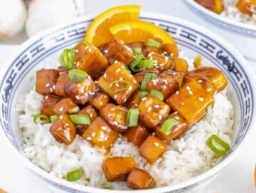 orange tofu with rice and green onions in a bowl