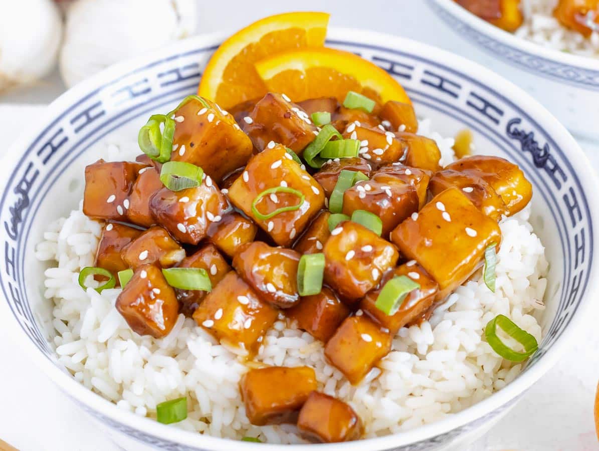 orange tofu with rice and green onions in a bowl