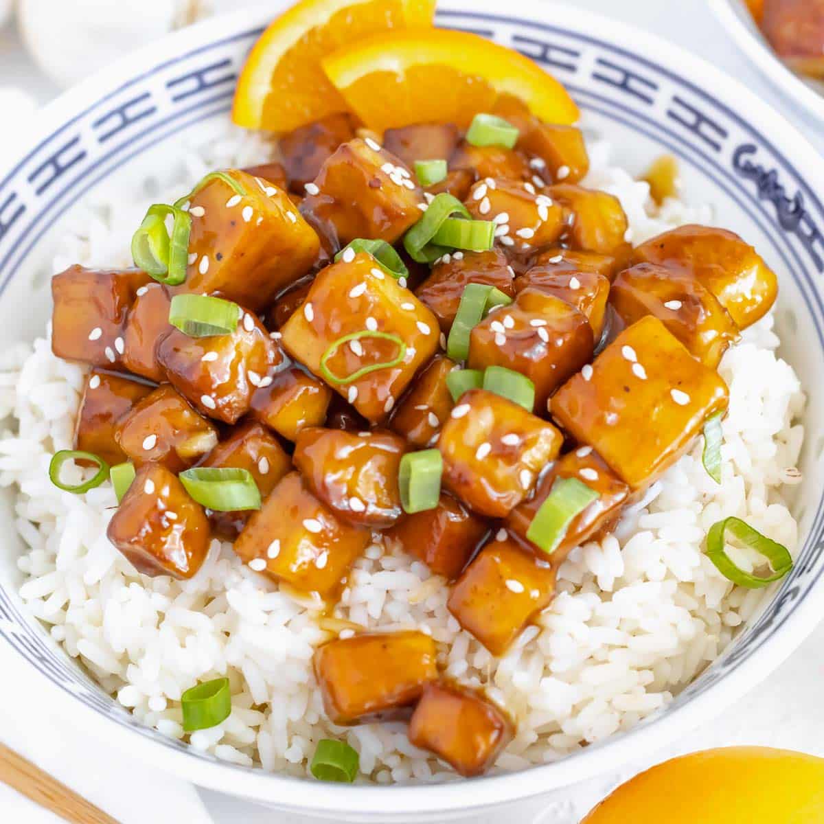 orange tofu served in a bowl on rice with spring onion.