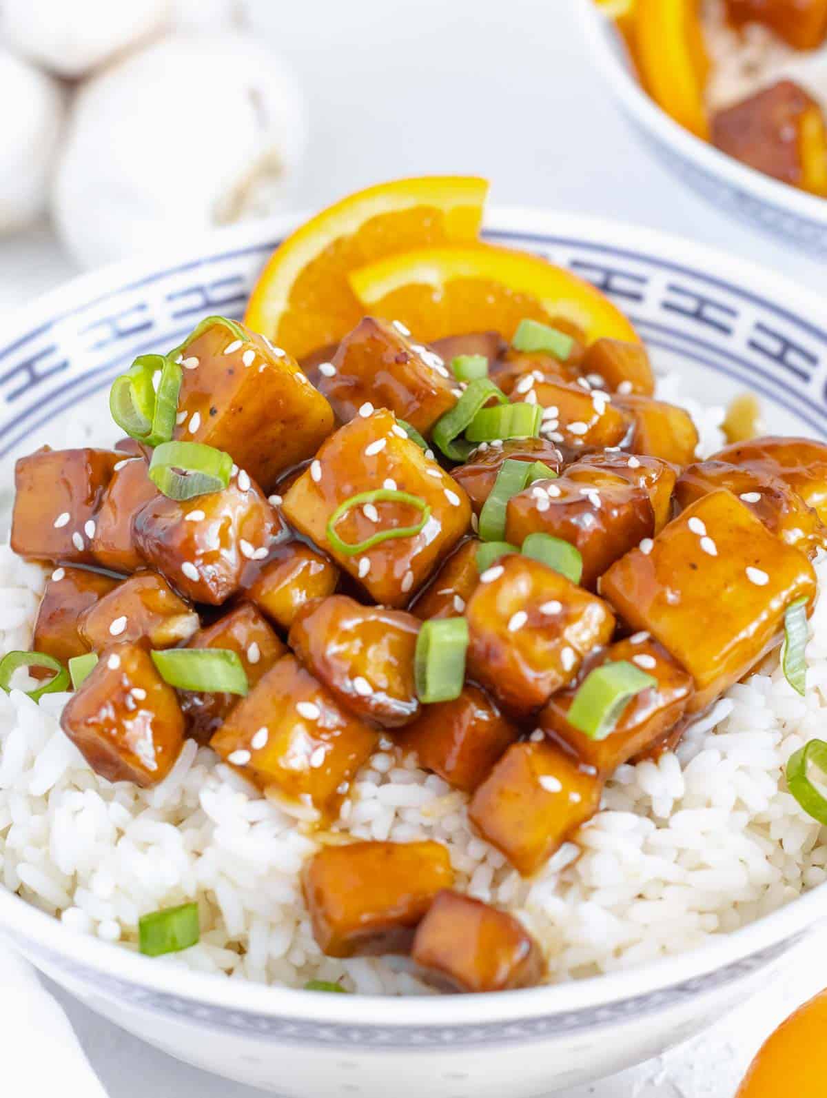 orange tofu in a bowl with spring onions on top