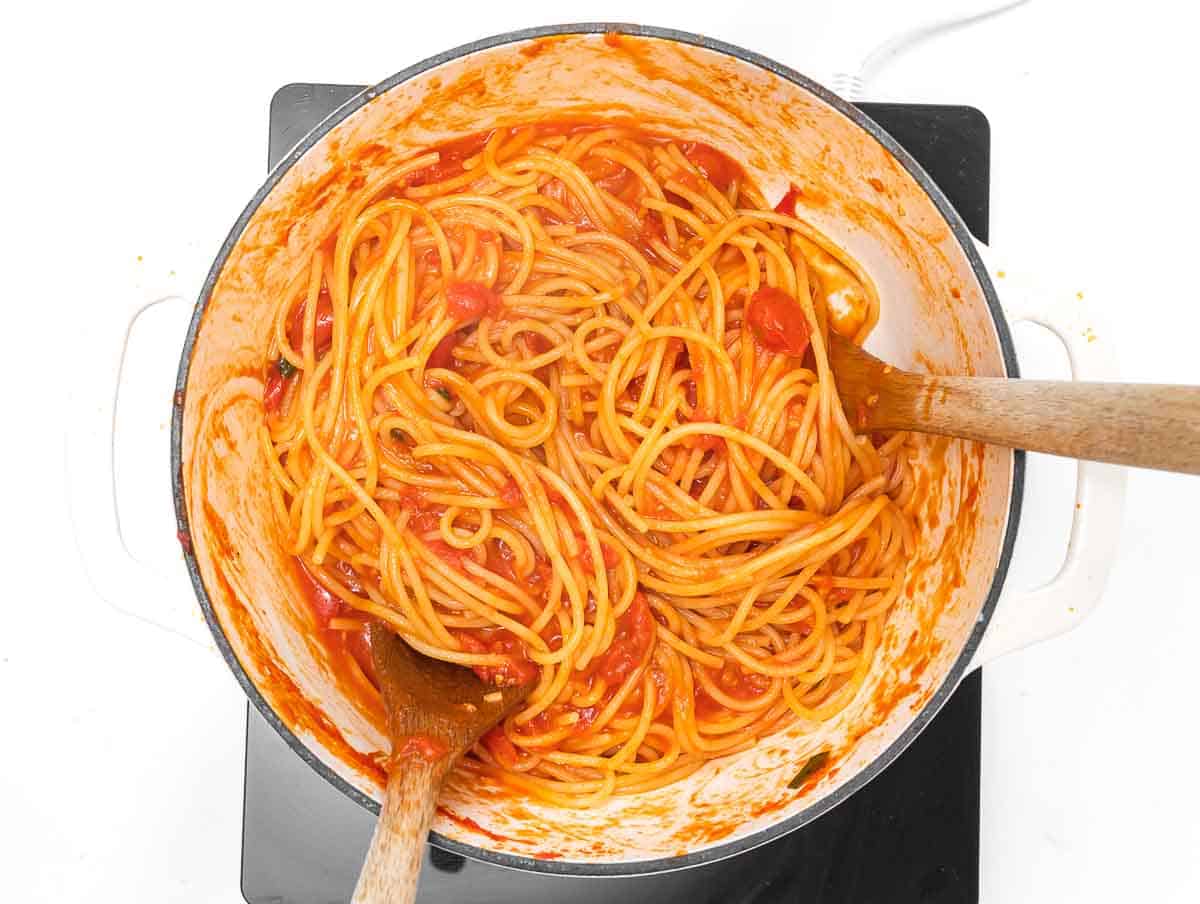tossing the spaghetti in the tomato sauce