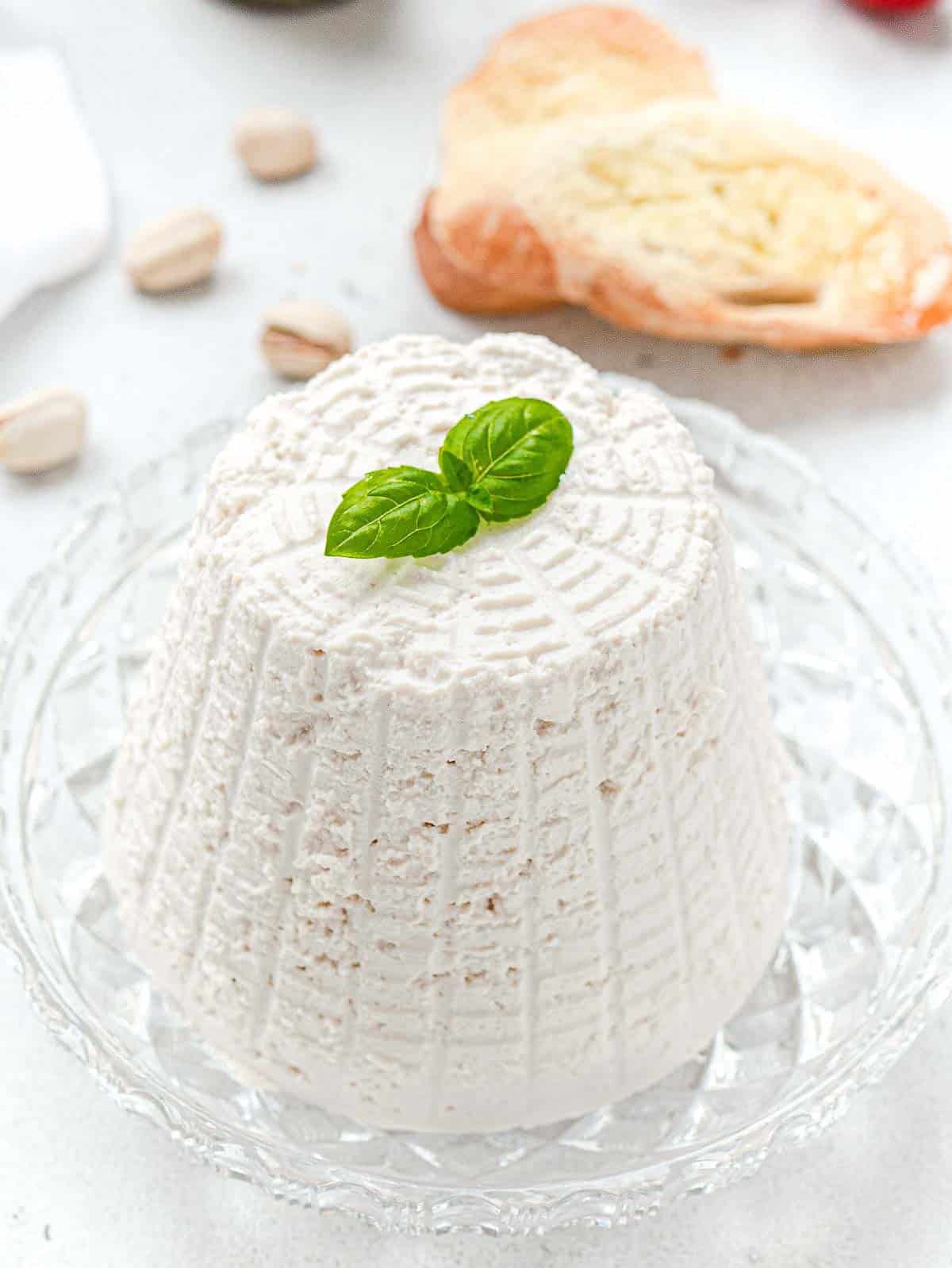 vegan ricotta cheese ready to be served with basil on top and slices of bread on the side.