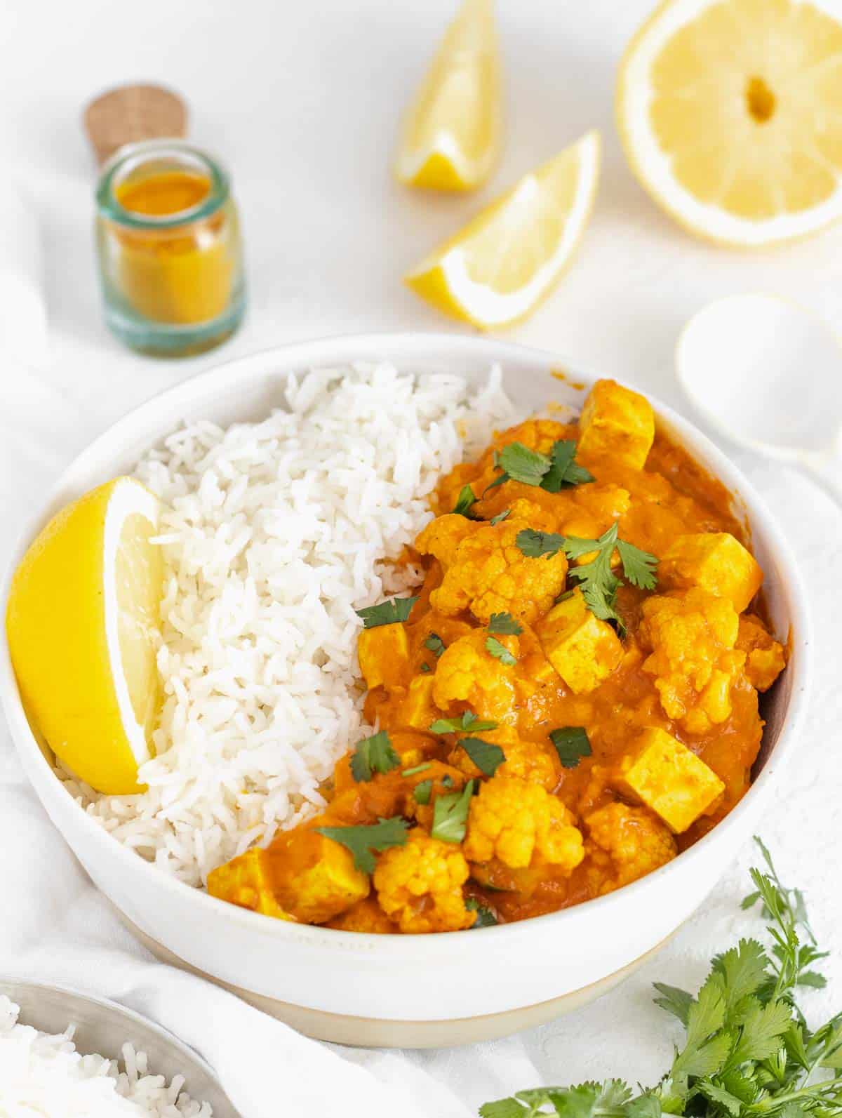 vegan curry served in a bowl with basmati rice, cilantro and lemon wedges