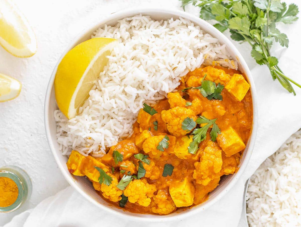 tofu curry served on basmati rice in a bowl, with a lemon wedge and cilantro.