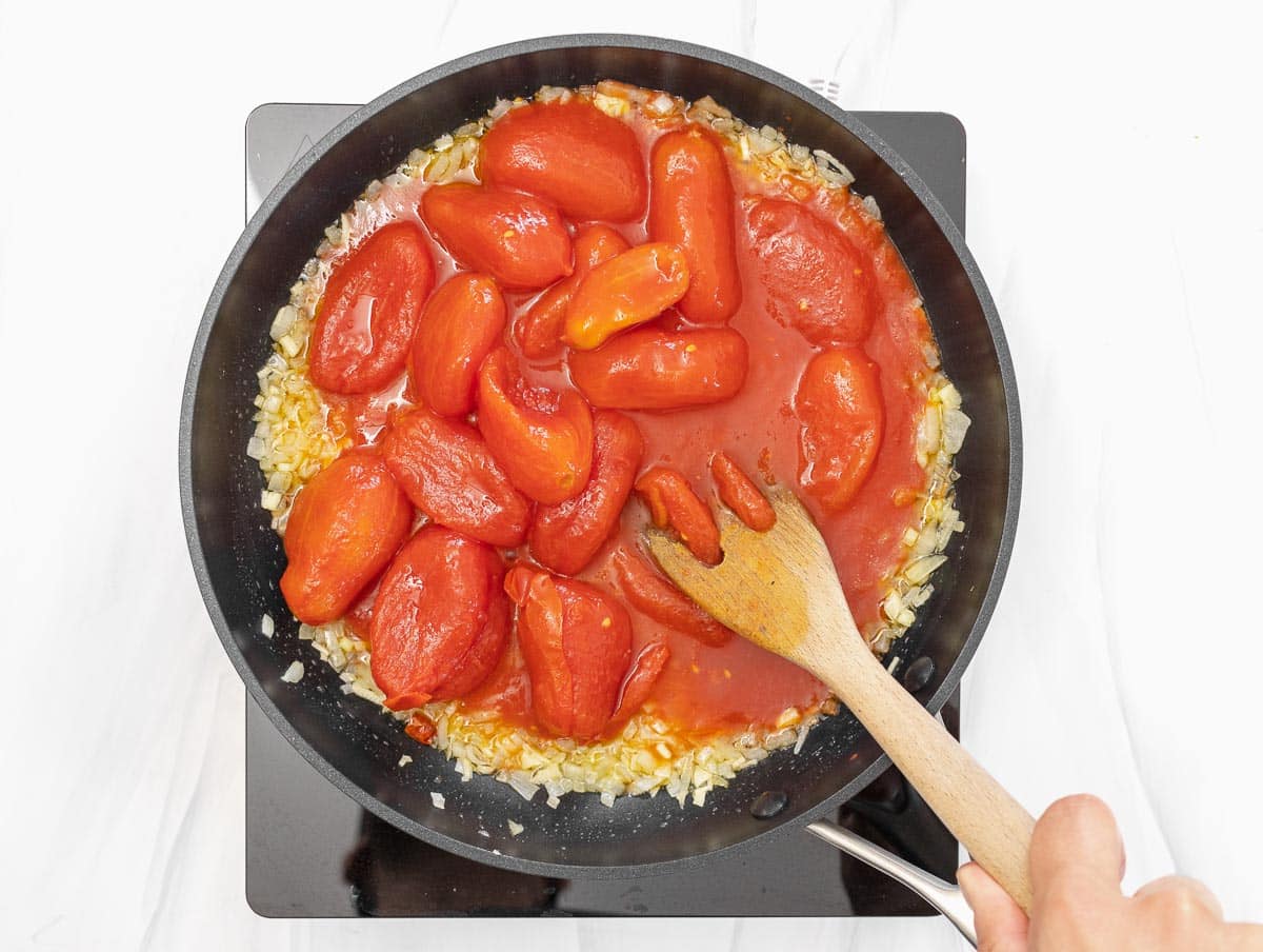 crushing whole canned peeled tomatoes with a wooden fork