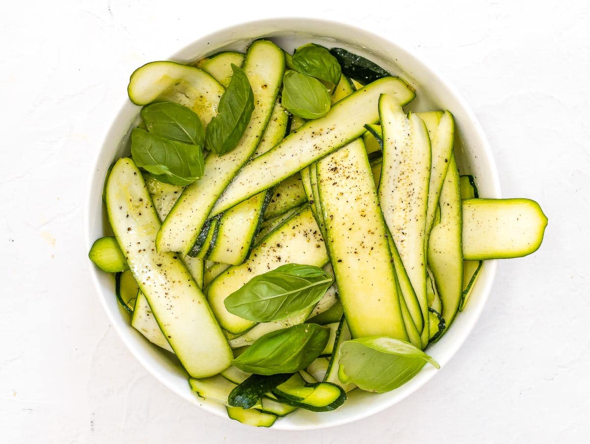 zucchini slices into a large bowl with basil, salt, and lemon juice
