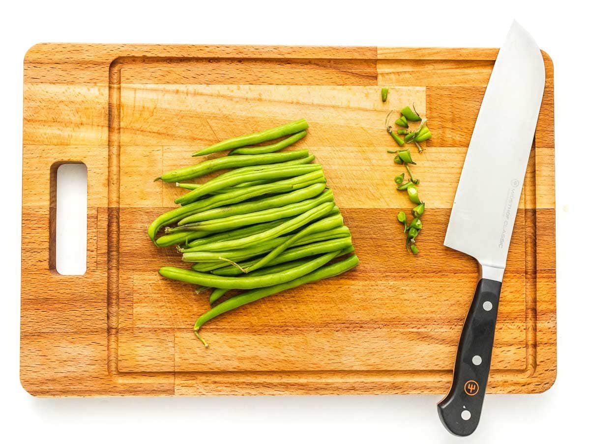 trimming green beans on a cutting board with a chef's knife