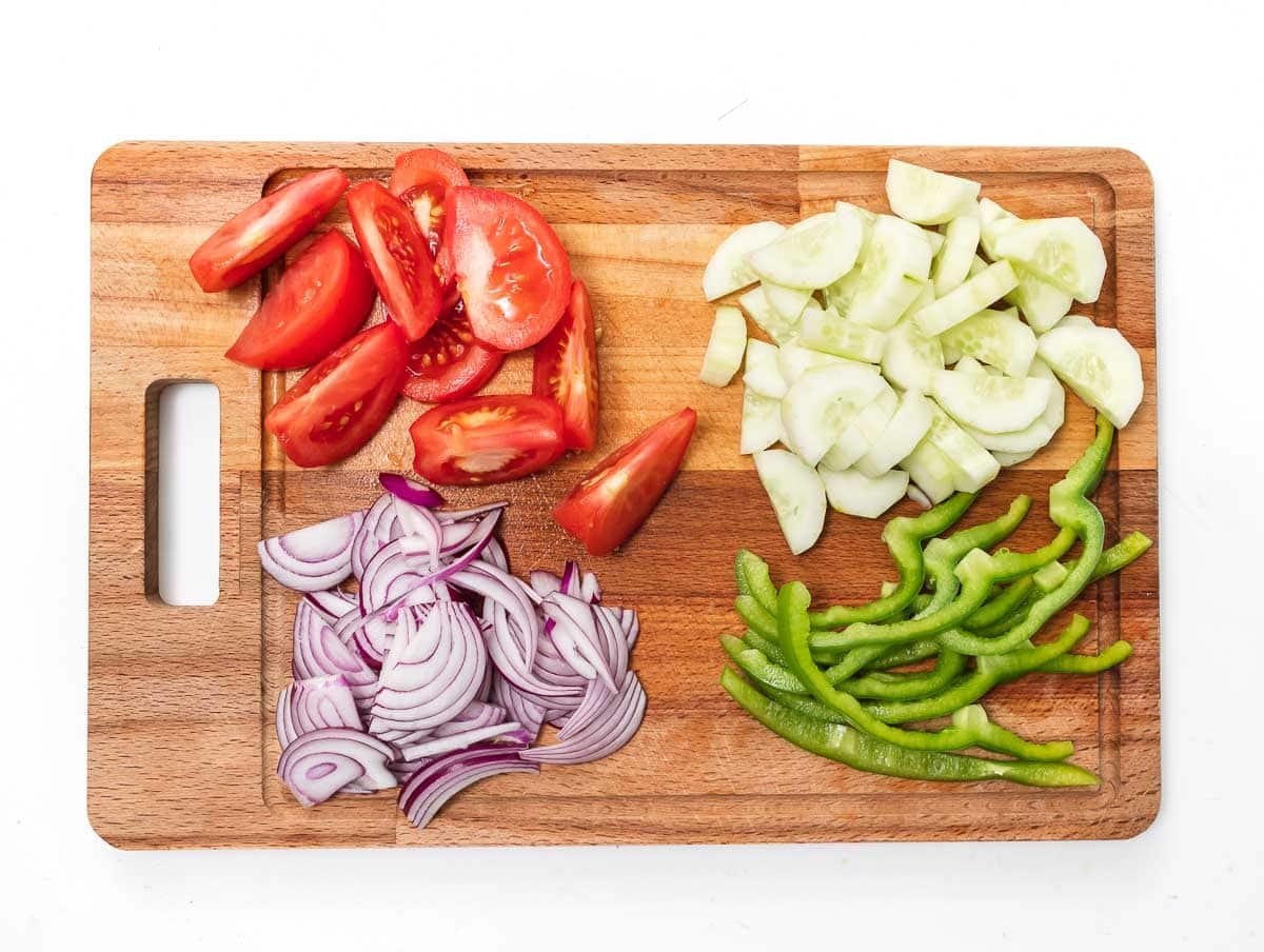 tomatoes, cucumber, red onion, and green pepper chopped on a cutting board