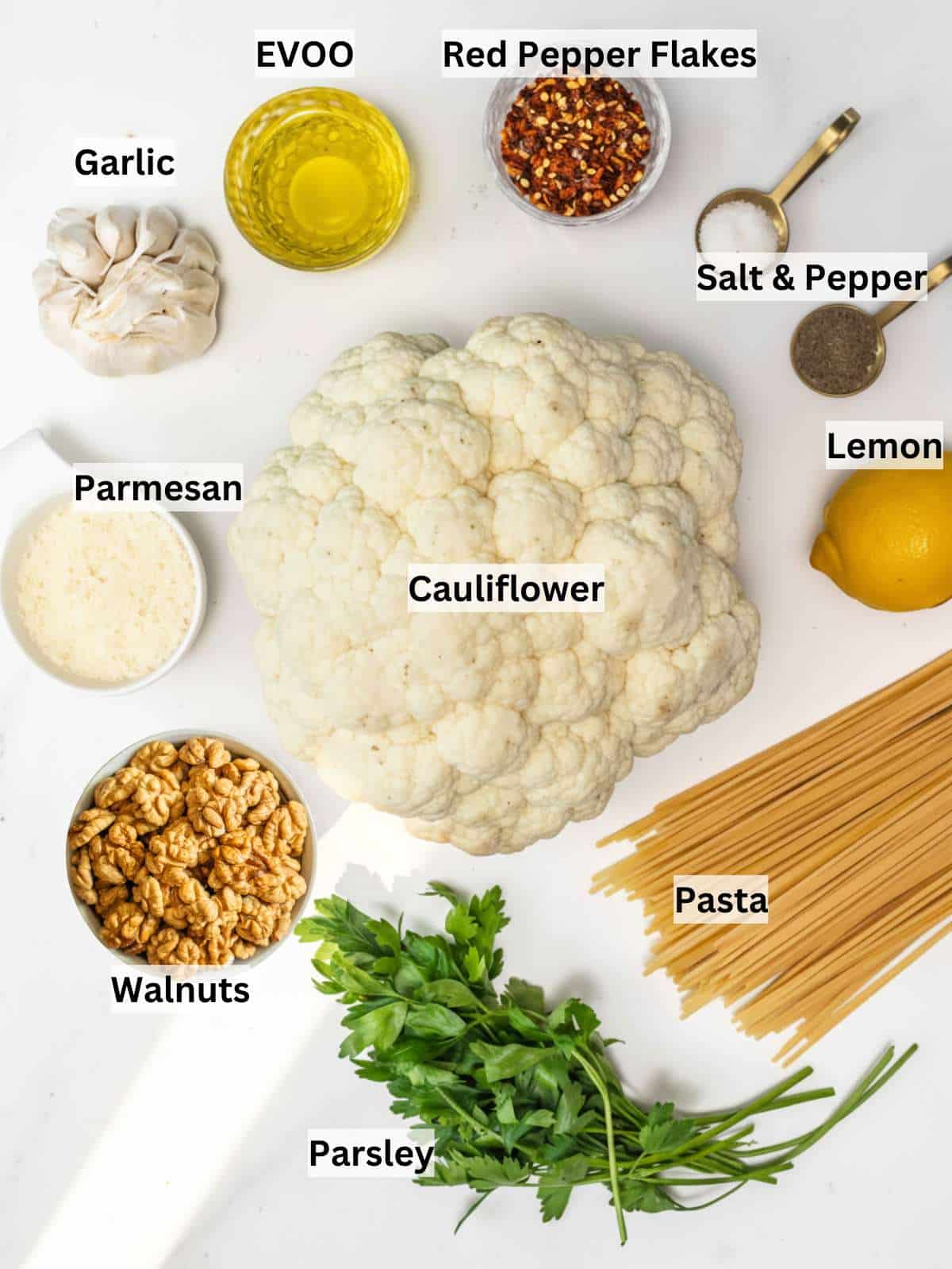 Ingredients for cauliflower pasta including spaghetti cauliflower garlic olive oil lemon parsley and nuts.