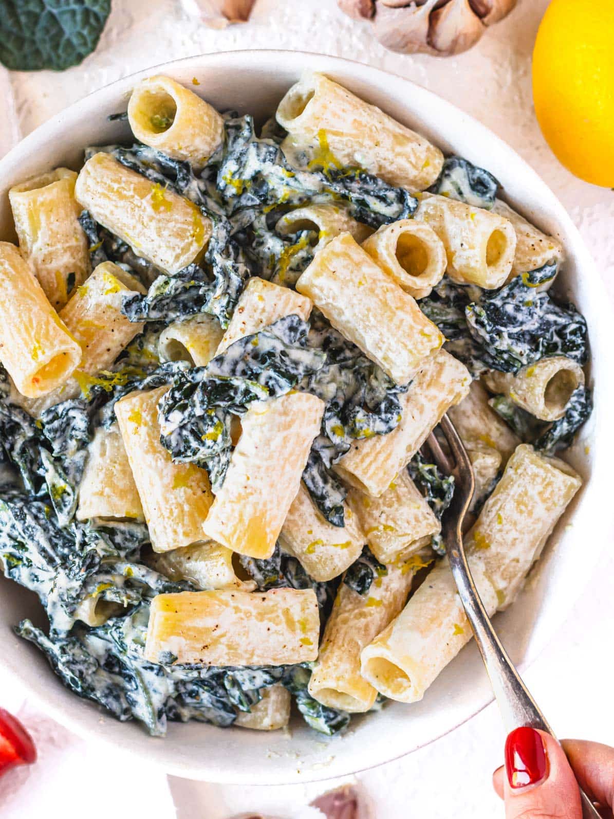 Kale pasta in a bowl with hand and a red nail