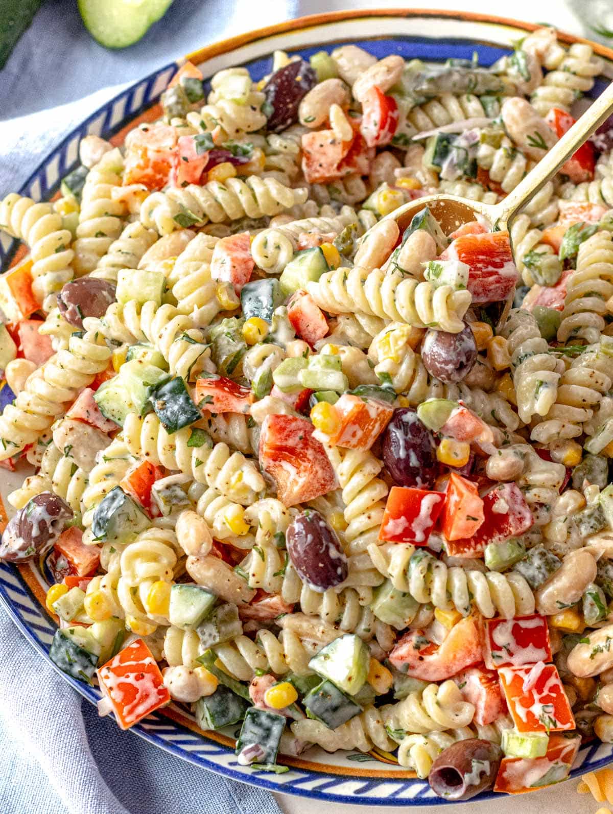 Creamy pasta salad on a plate with fresh veggies and parsley in the background