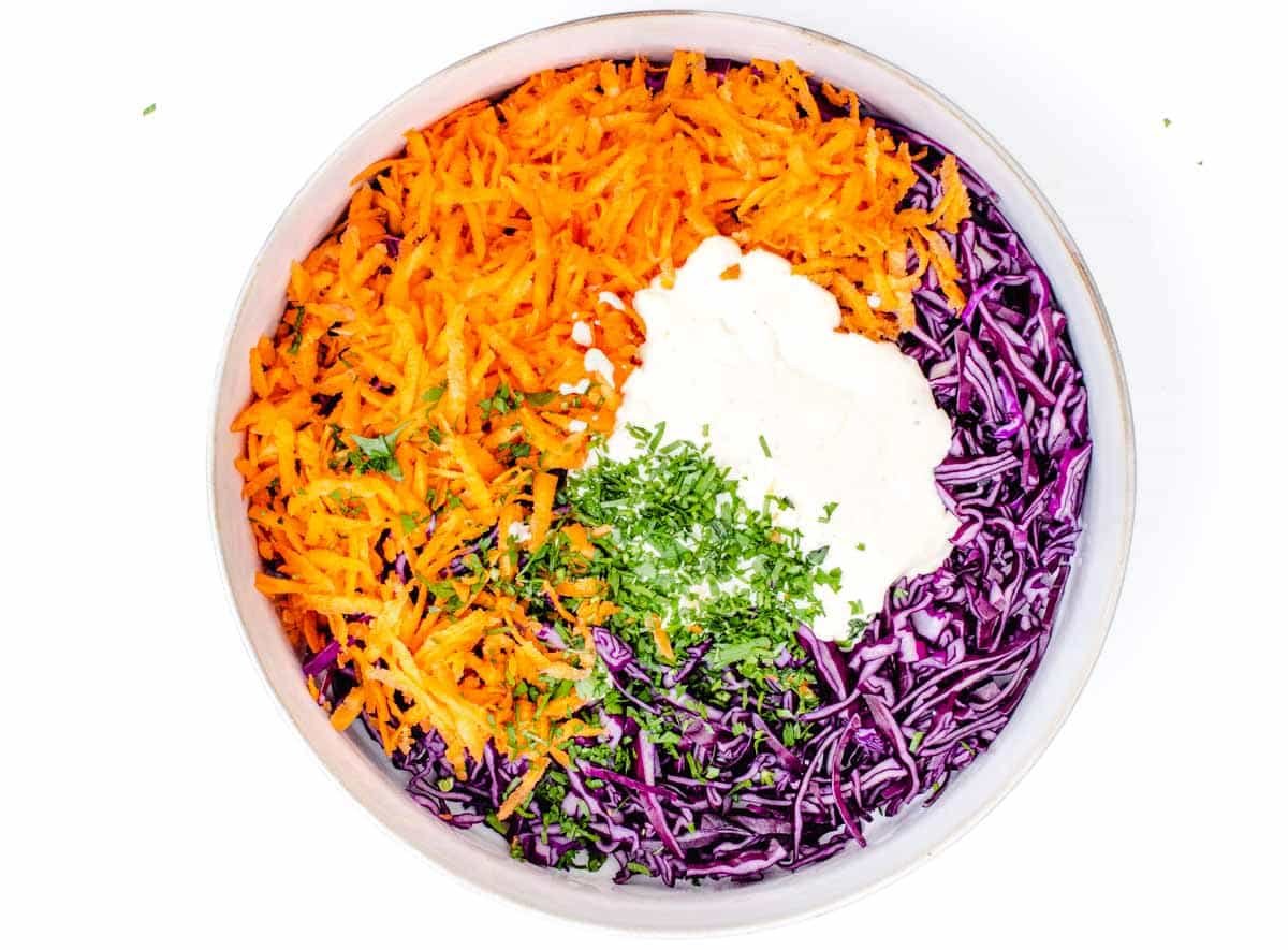 purple cabbage, shredded carrot, parsley, and dressing in a bowl