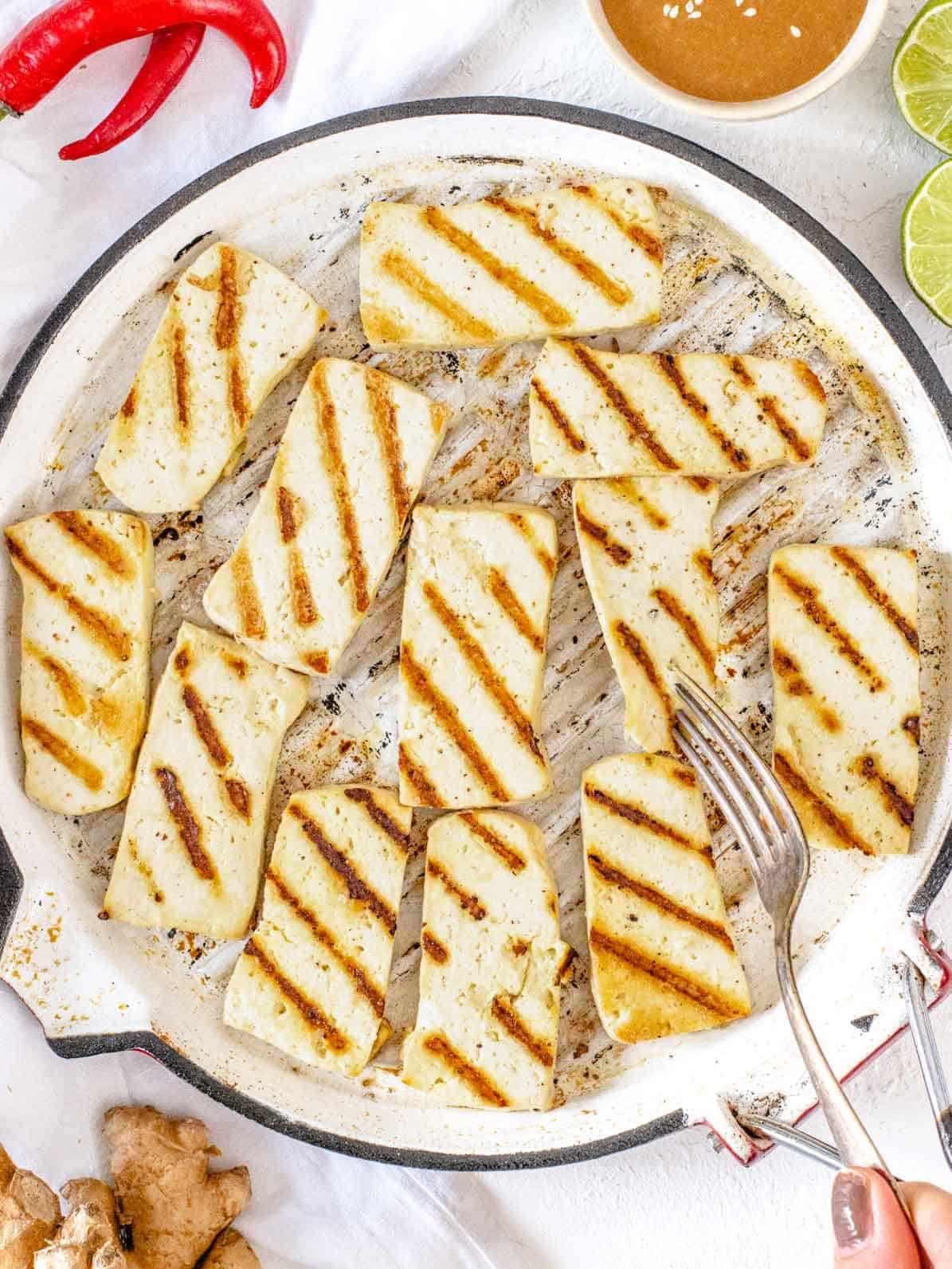 Grilled tofu on a pan with fork and a hand