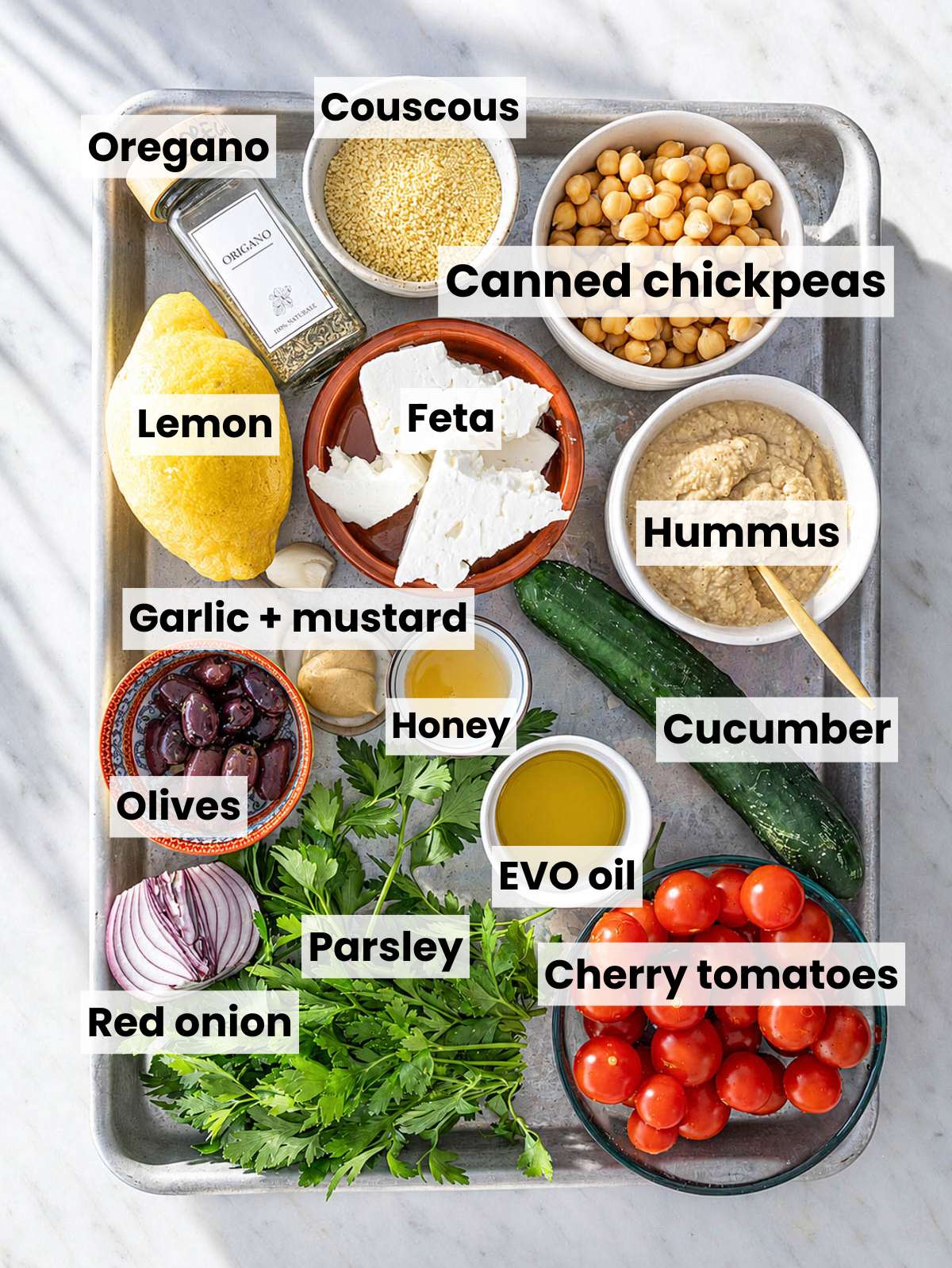 Mediterranean Bowl ingredients on white marble with fresh vegetables, chickpeas, feta, and pita.