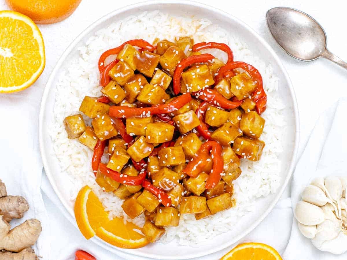 orange tofu with bell peppers served on a bowl of rice