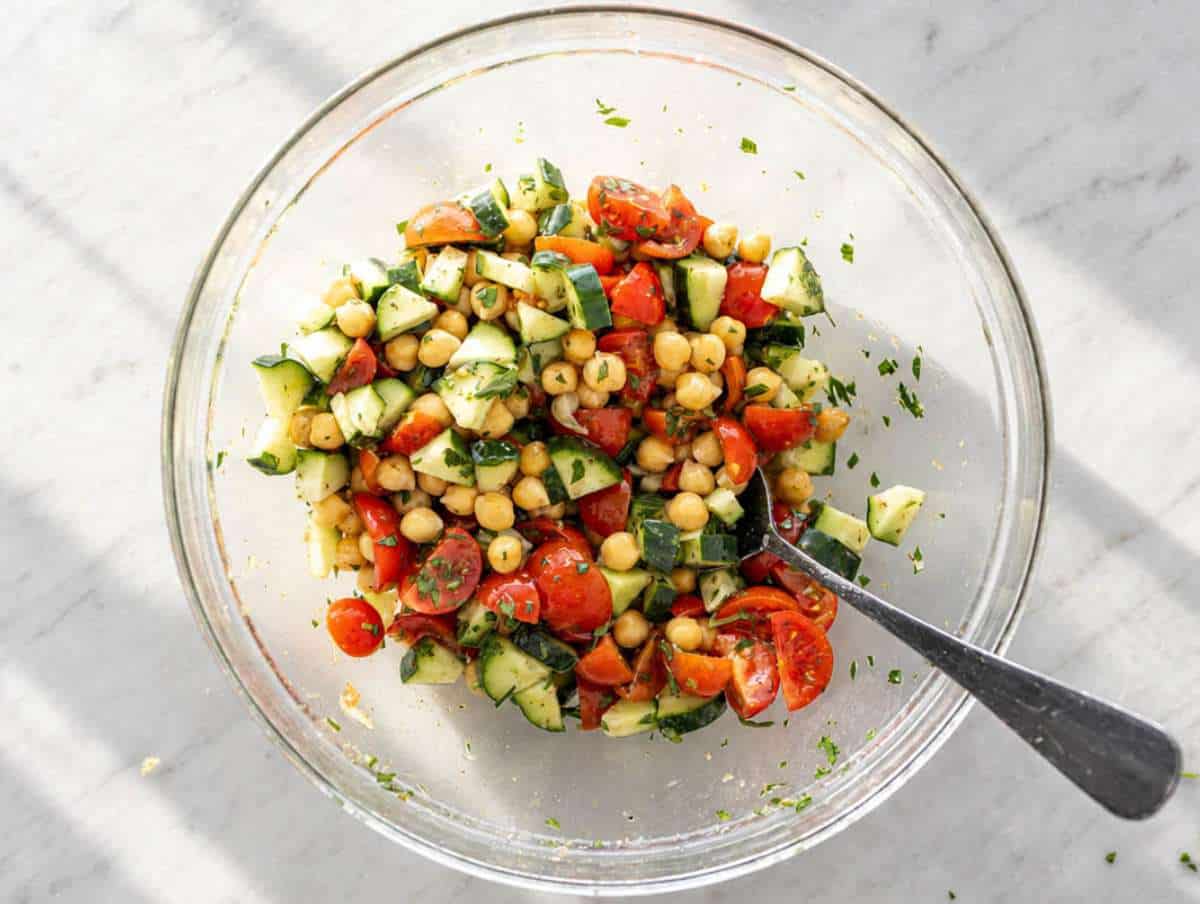 Step 2 Tossing marinated chickpeas with cucumber, tomatoes, and chopped parsley until combined.