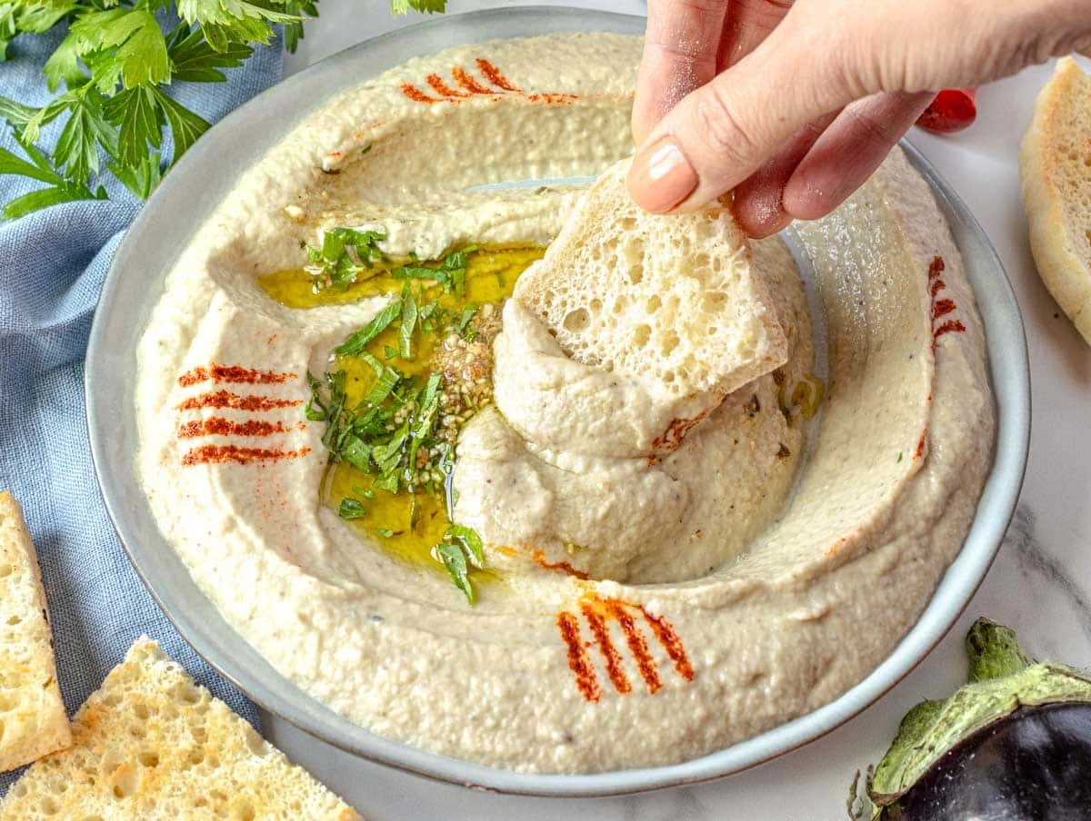 Baba ganoush on a small plate with hand holding a pita bread
