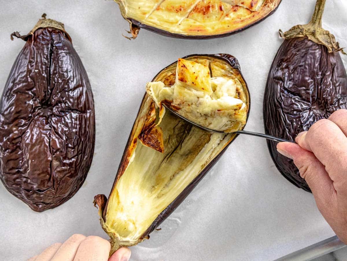 hands using a spoon to remove flesh from roasted eggplant