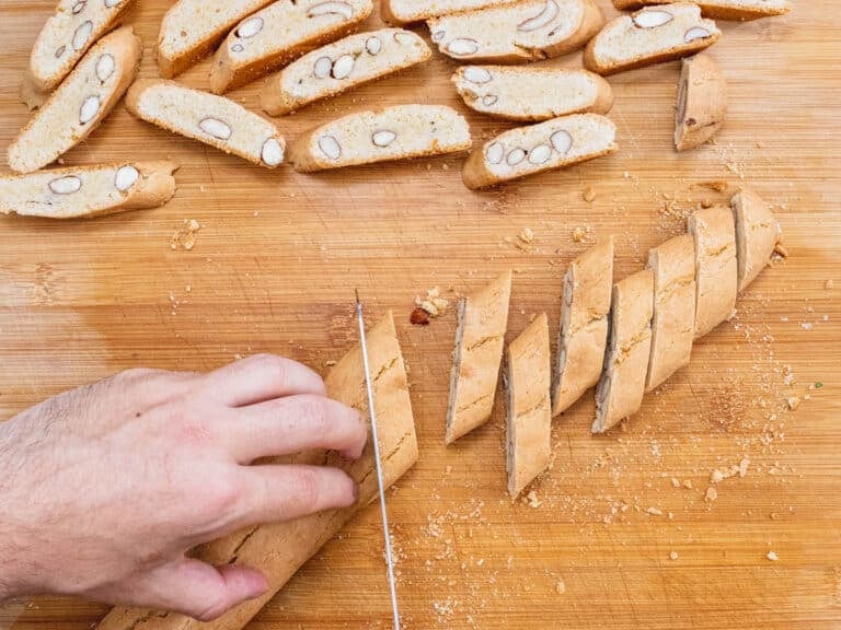 hands and serrated knife cutting biscotti