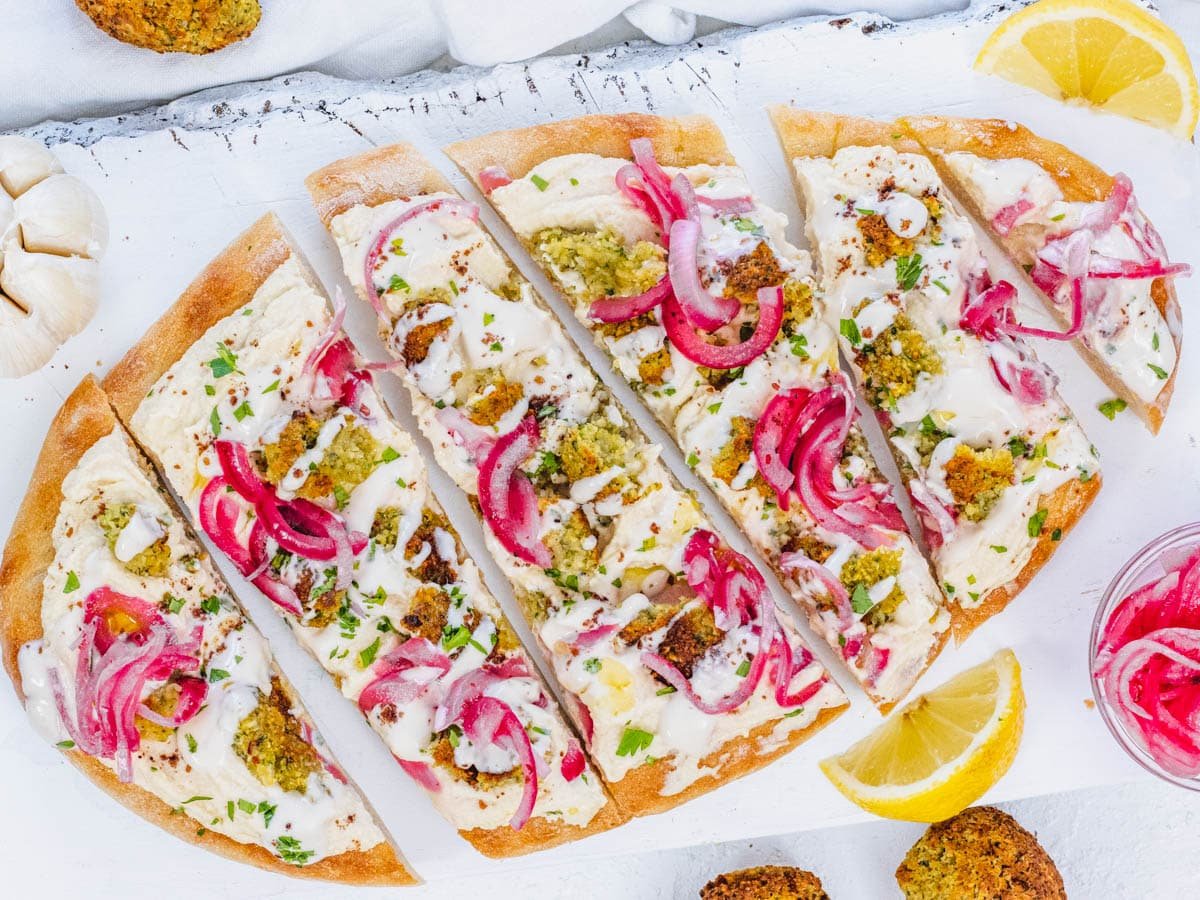 flatbread pizza with hummus, falafel, tahini sauce, and pickled onions