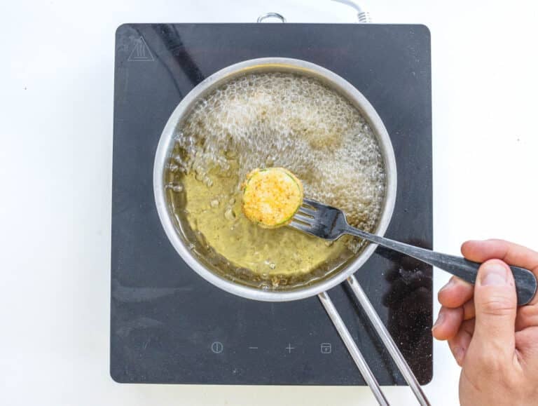 Zucchini frying in oil and a hand with a fork
