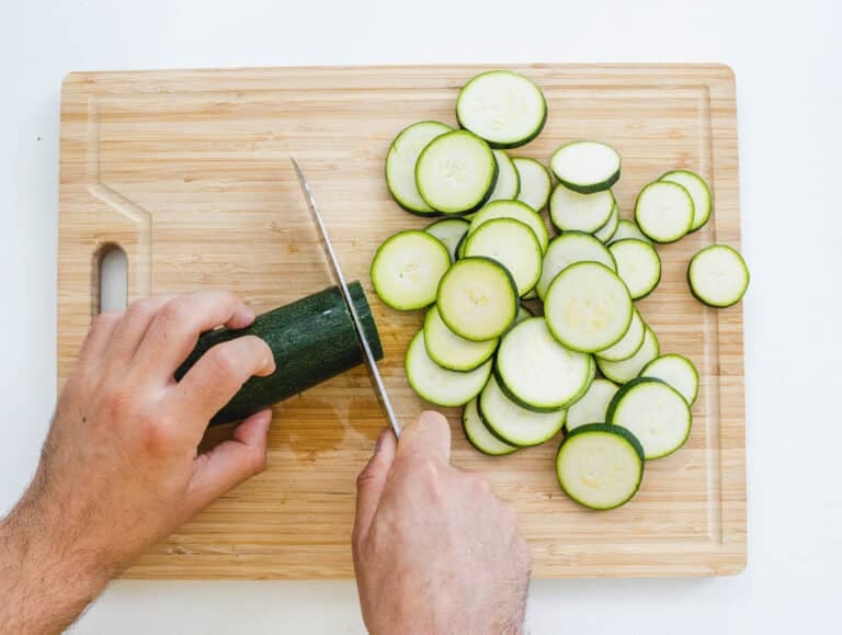 Hands and knife slicing a zucchini