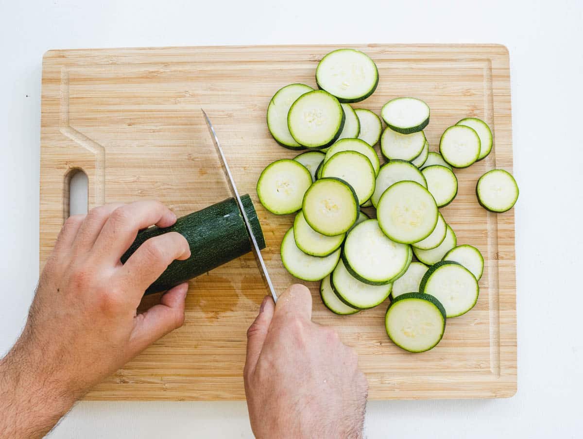 Hands and knife slicing a zucchini