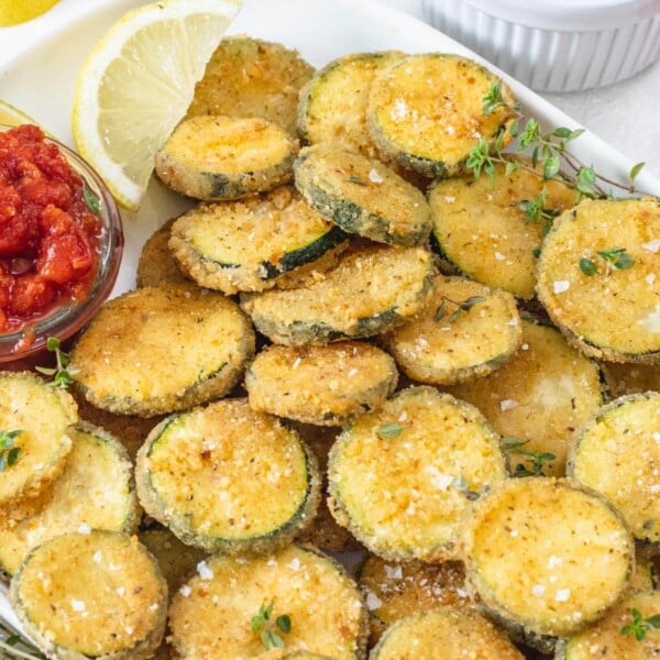 Fried zucchini on a platter with a lemon wedge