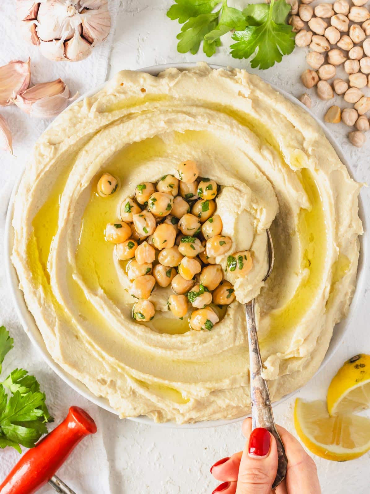 Hummus on a plate with chickpeas in the middle and a hand holding a spoon