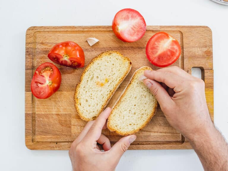 Hands with garlic on white bread and tomatoes