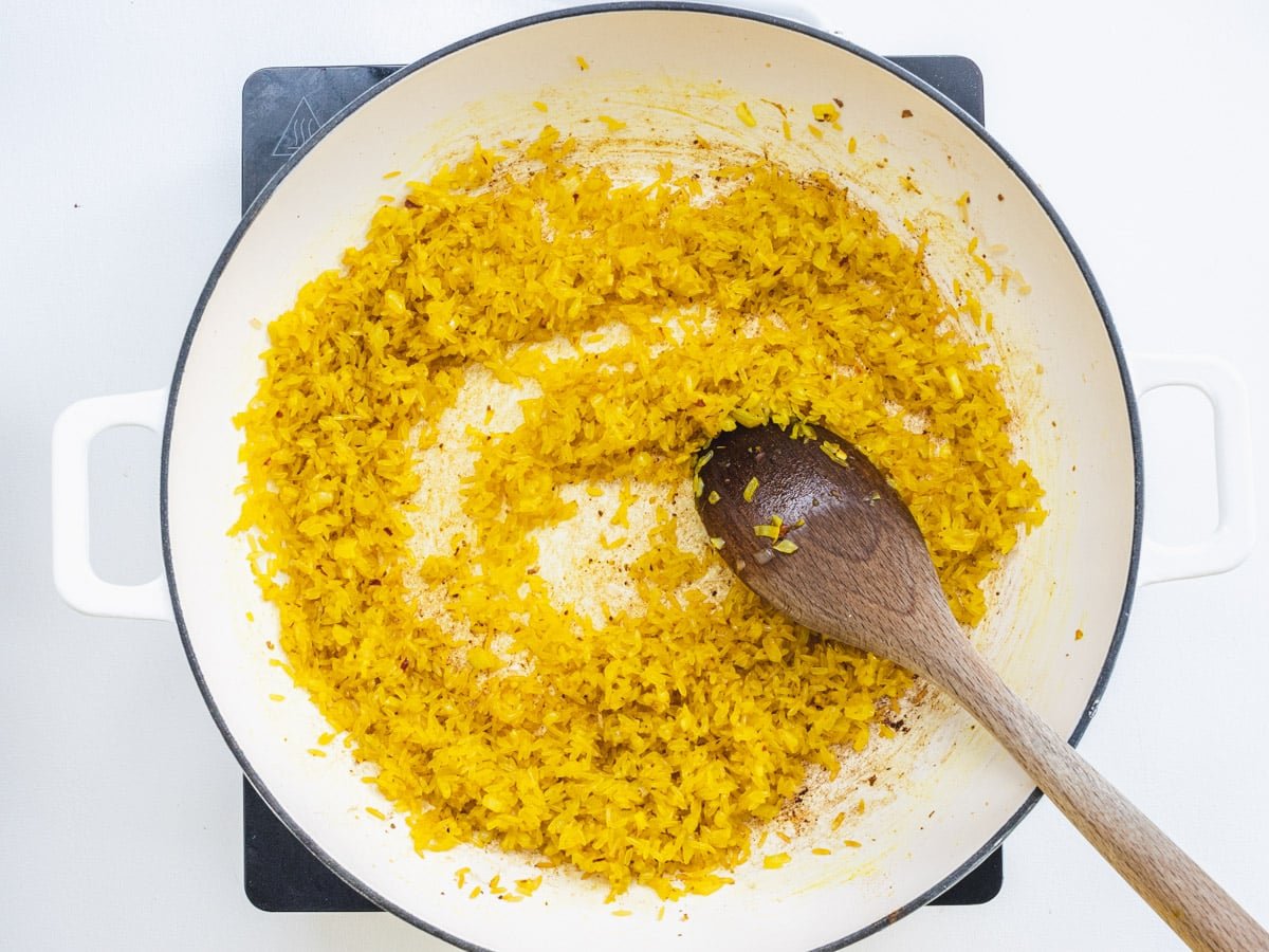 Rice, turmeric and onion in a white skillet