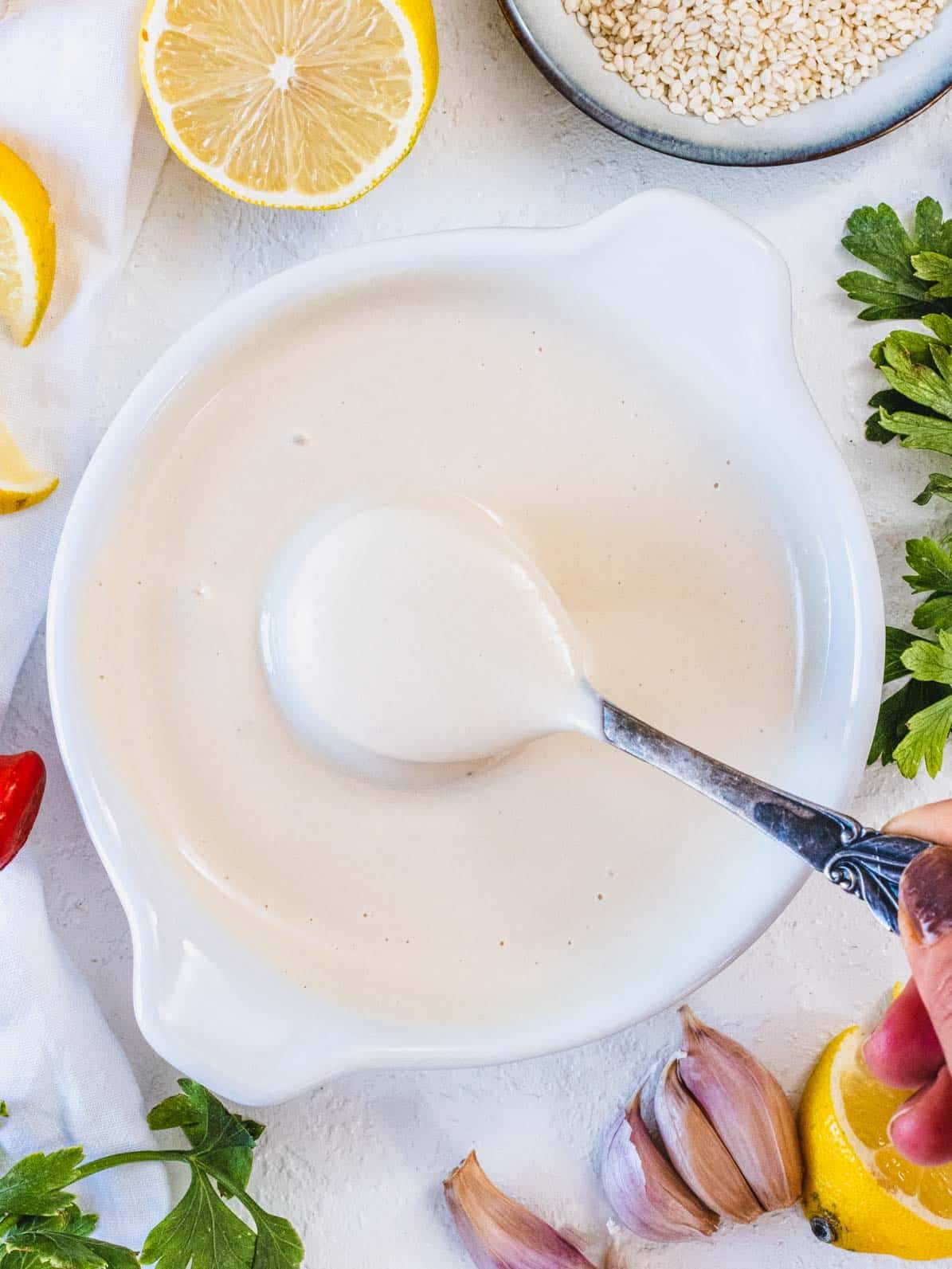 tahini sauce in a white bowl with silver spoon