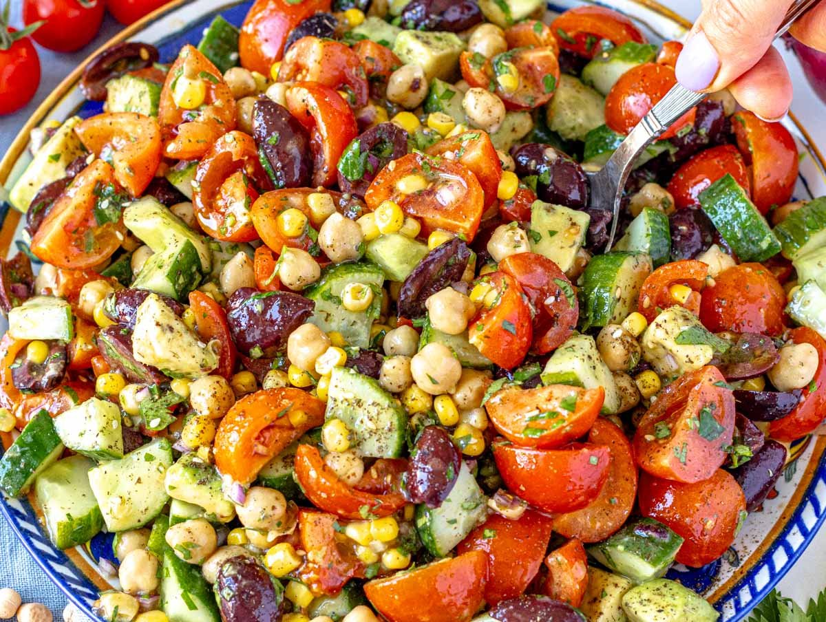 Chickpea salad recipe on a blue plate with hand holding a spoon