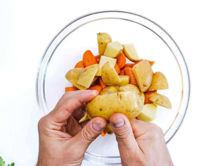 hands cutting potatoes and carrots into a bowl