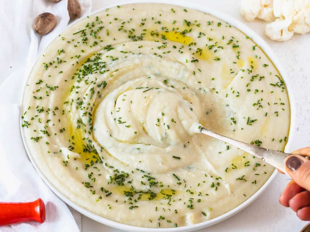 Cauliflower potato mash with hand holding a spoon