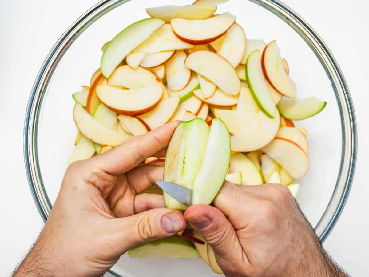 hands and a knife slicing apple into a casserole