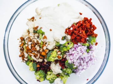 broccoli cauliflower, dressing, nuts, and red onions in a glass bowl