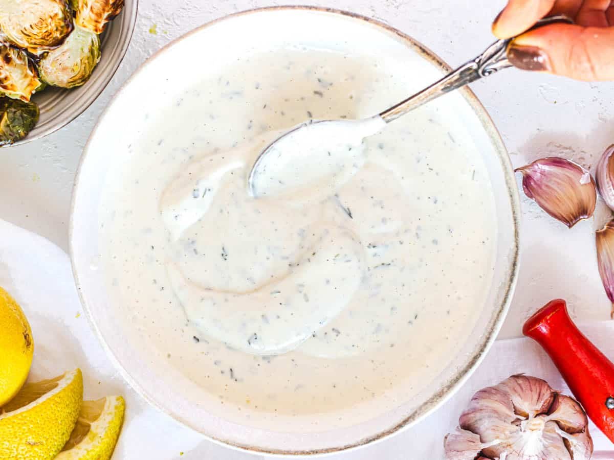 vegan ranch dressing with hand and silver spoon
