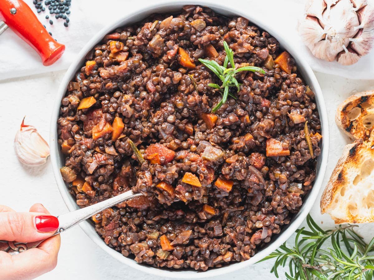 Black lentils with a spoon and hand with red nail