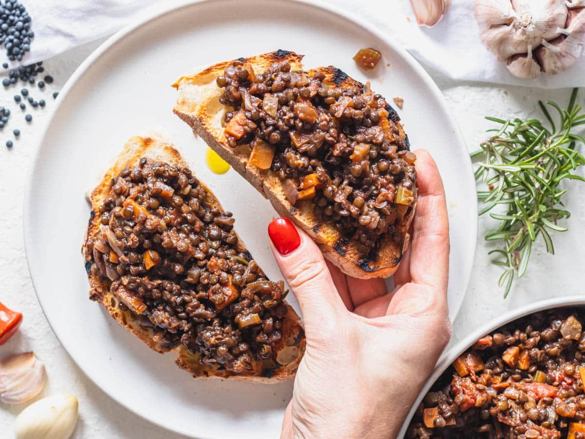 Black lentils on bruschetta with hand and a red nail