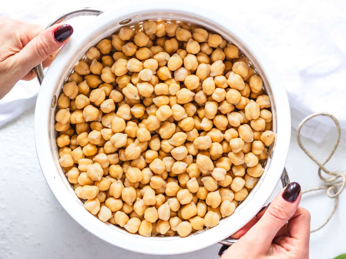 Dried chickpeas before cooking in a white sift with two hands