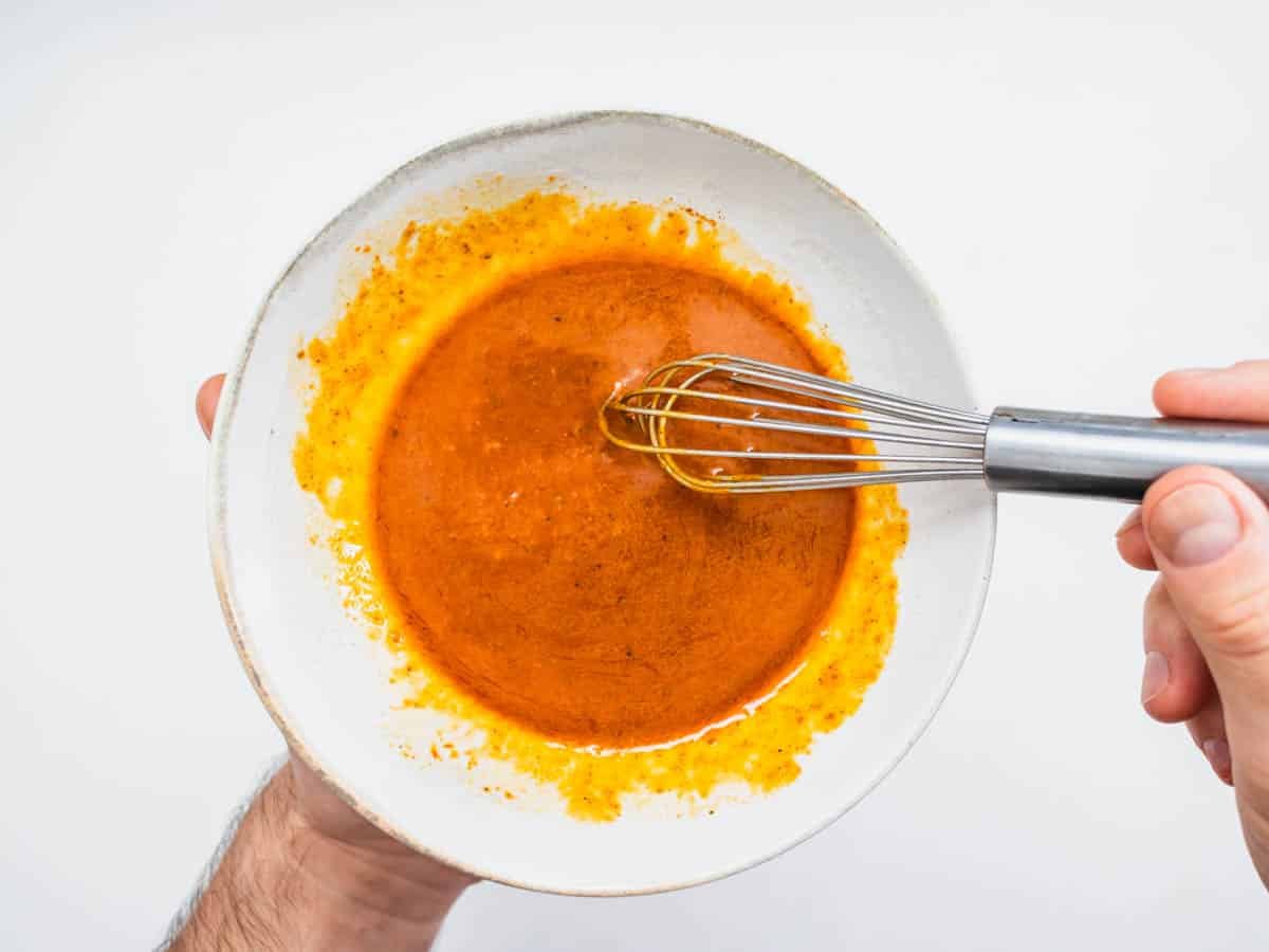 harissa dressing in a small bowl with hands and a whisk
