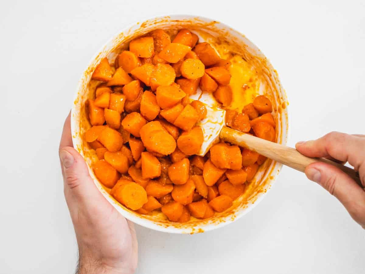 hands mixing carrots with a harissa dressing