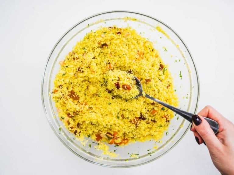 yellow couscous with dried fruits and almonds in a glass bowl with a hand