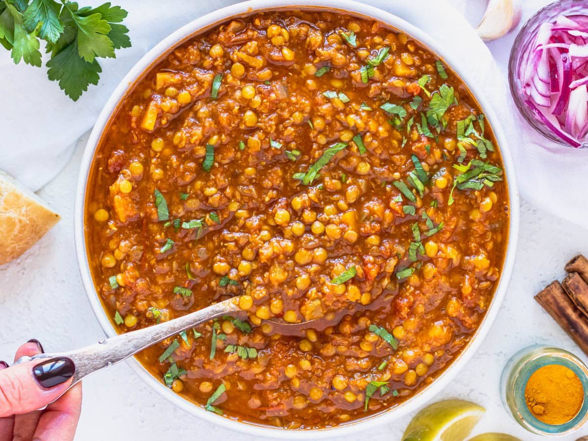 Moroccan lentil soup with hand holding a silver spoon