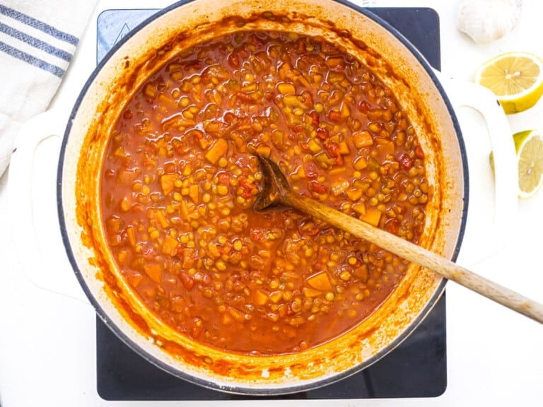 cooked lentils in a tomato broth with a wooden spoon